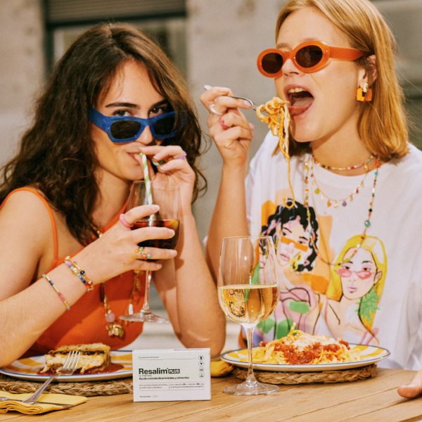 Chicas comiendo pasta y tomando vino posando junto a una caja de Resalim